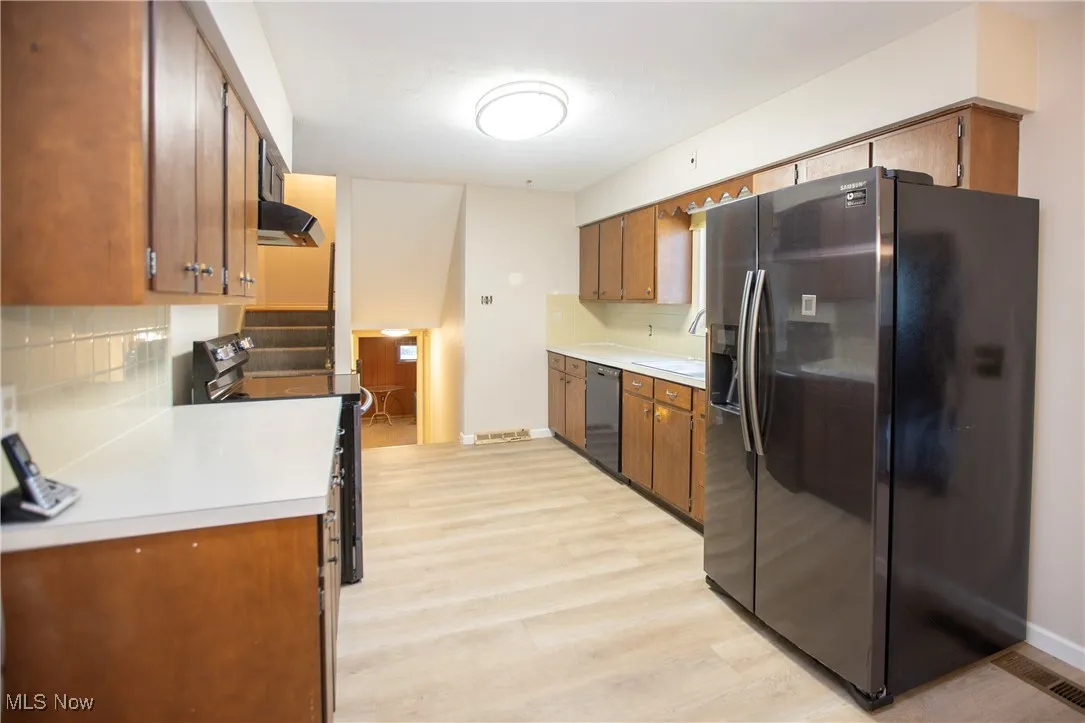 Kitchen with black refrigerator with ice dispenser, backsplash, light countertops, range with electric stovetop, and brown cabinets
