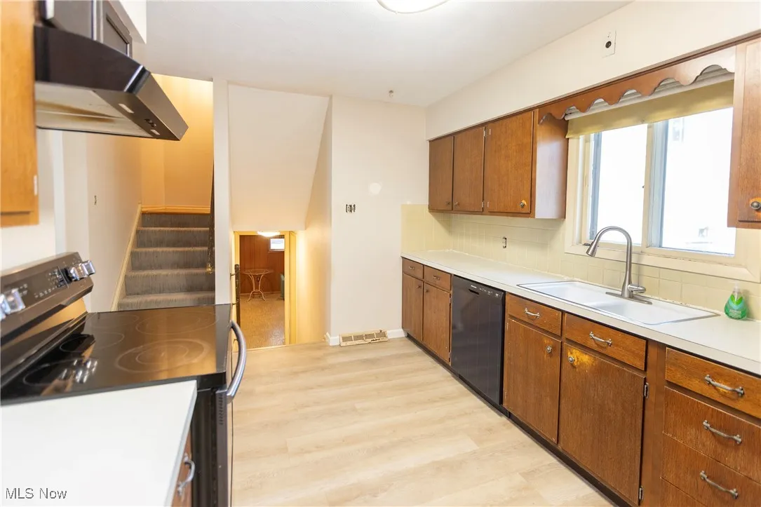 Kitchen with stainless steel range with electric stovetop, under cabinet range hood, light countertops, black dishwasher, and light wood-style flooring