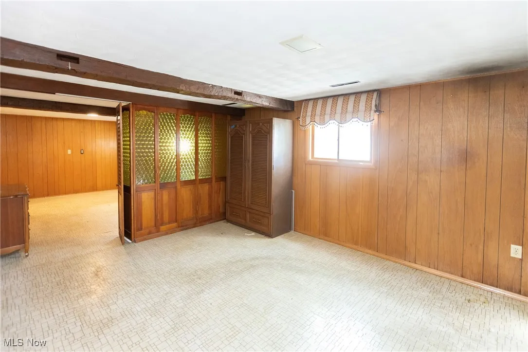 Spare room with wooden walls, beamed ceiling, and light floors