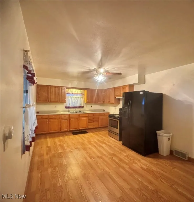 Kitchen with black refrigerator with ice dispenser, light wood finished floors, stainless steel electric range, light countertops, and brown cabinetry