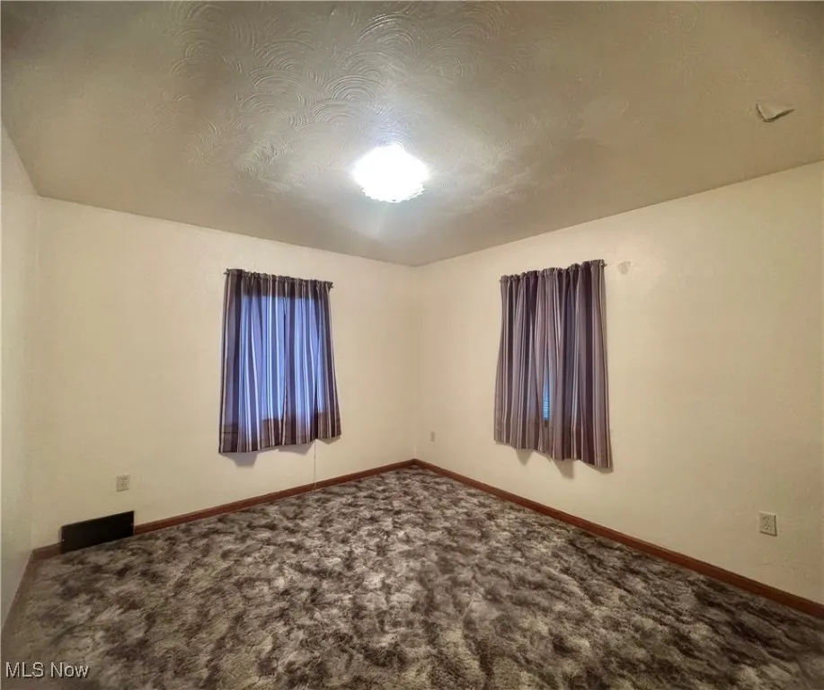 Carpeted empty room featuring a textured ceiling and baseboards