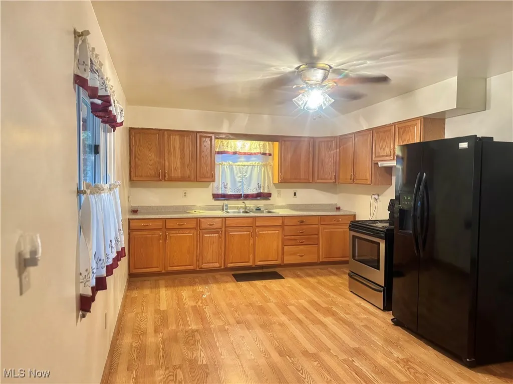 Kitchen with black fridge, light countertops, stainless steel electric range, light wood finished floors, and brown cabinetry