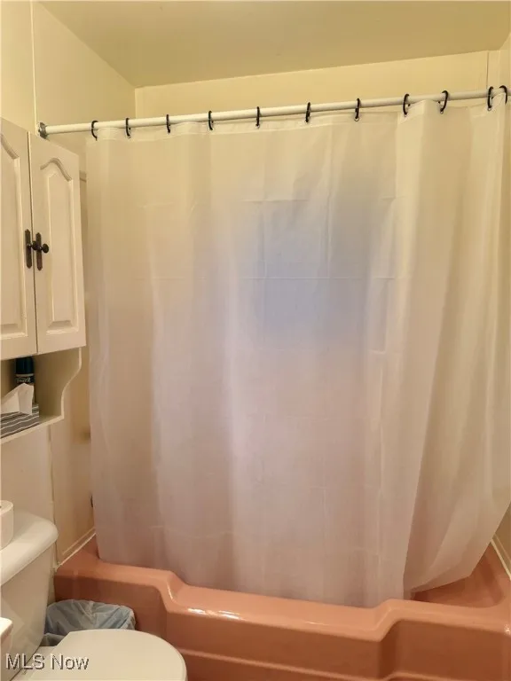 Bathroom featuring shower / bathtub combination with curtain and toilet
