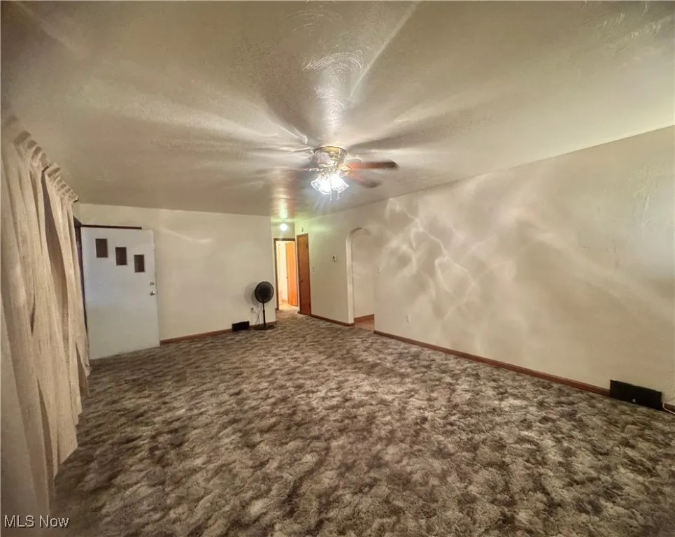 Spare room featuring a textured ceiling, arched walkways, dark colored carpet, and ceiling fan