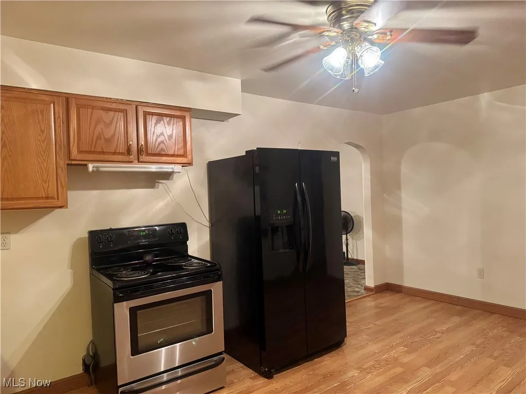 Kitchen featuring stainless steel electric range oven, black fridge with ice dispenser, brown cabinets, light wood-style flooring, and a ceiling fan