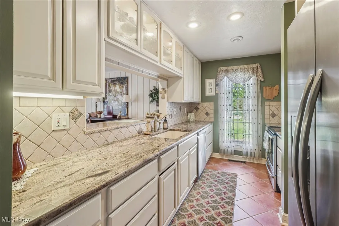 Kitchen with stainless steel appliances, glass insert cabinets, light tile patterned floors, decorative backsplash, and light stone countertops