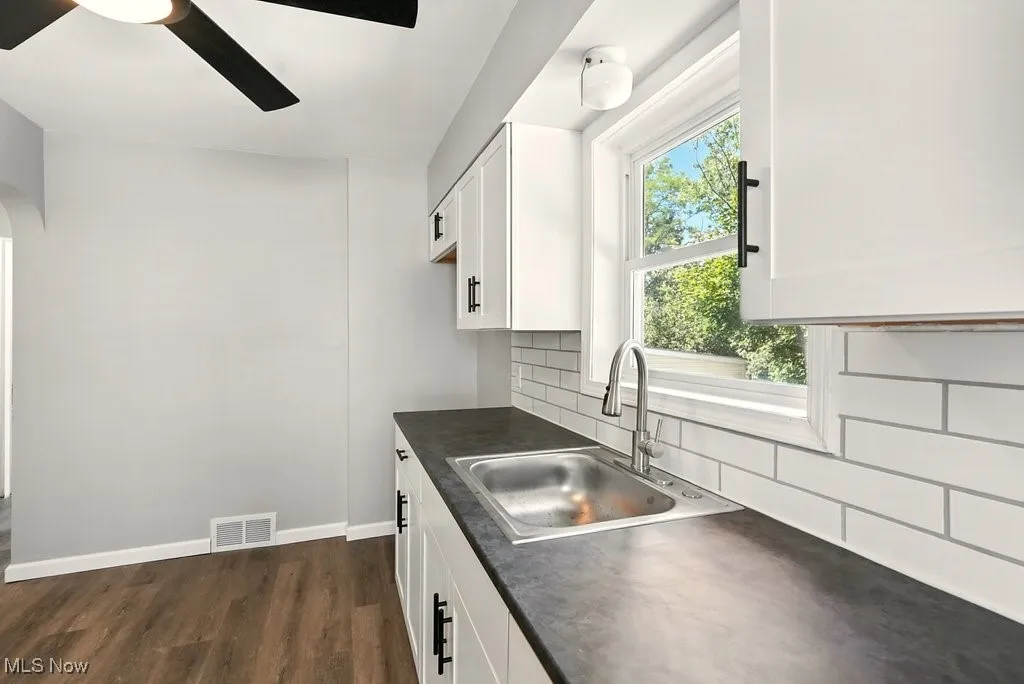 Kitchen with white cabinets, dark countertops, dark wood-style floors, backsplash, and ceiling fan