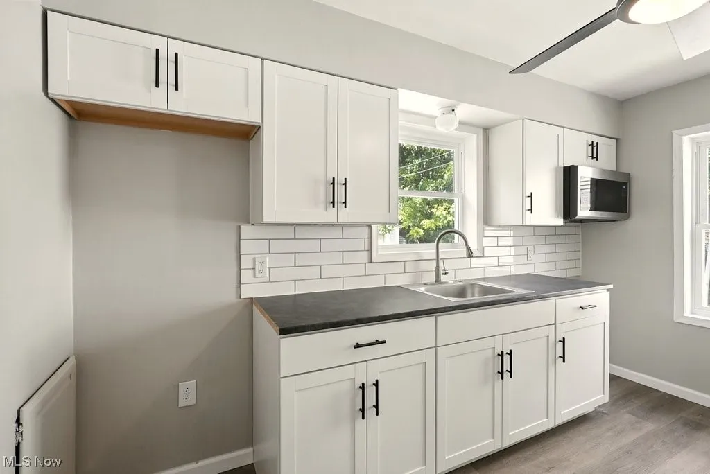 Kitchen with tasteful backsplash, dark countertops, stainless steel microwave, and white cabinets