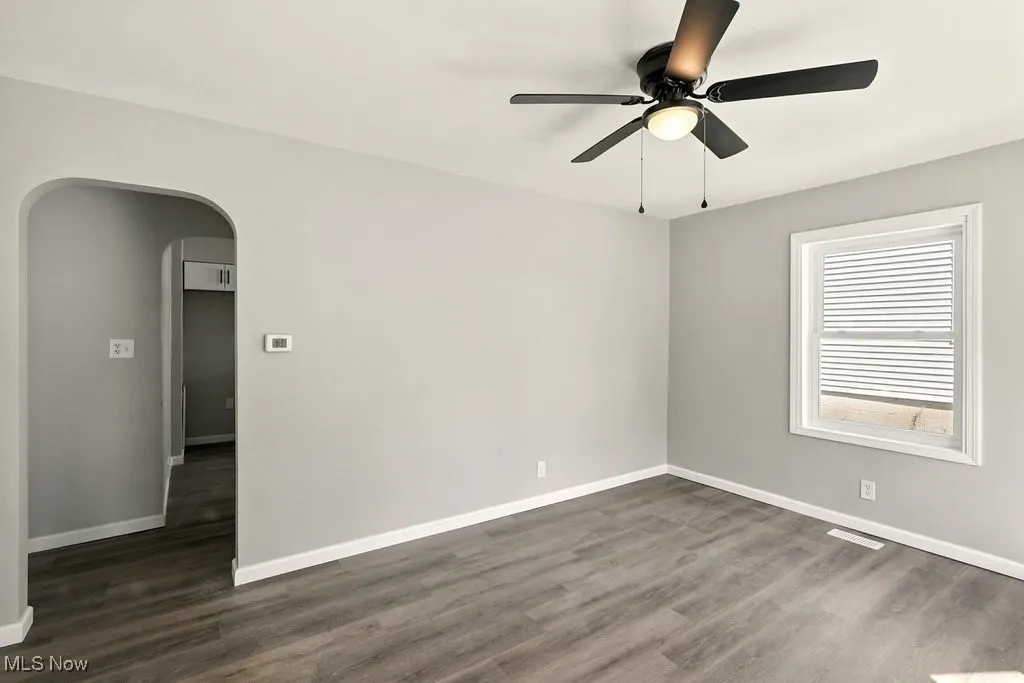 Living room featuring arched walkways, dark wood-style floors, and ceiling fan