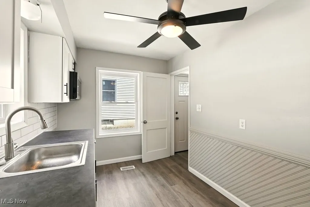 Kitchen featuring dark wood-style floors, dark countertops, white cabinetry, tasteful backsplash, and black microwave