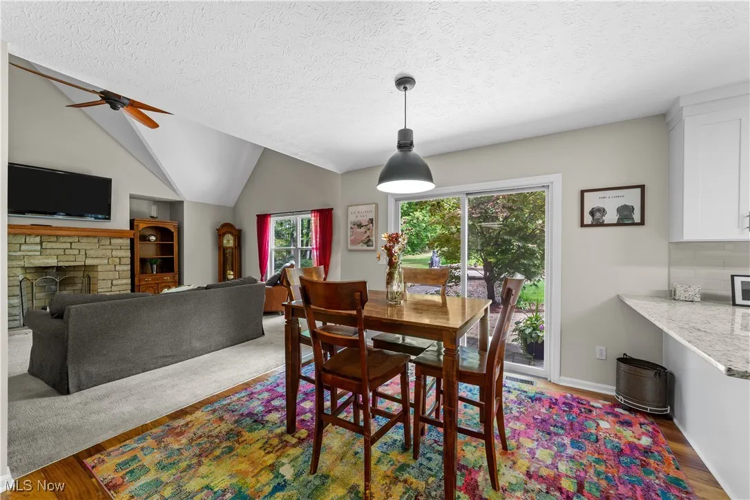 Dining area with wood finished floors, lofted ceiling, a textured ceiling, a fireplace, and a ceiling fan