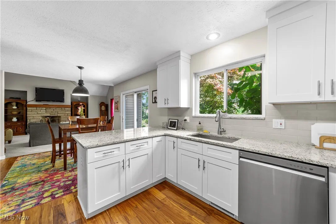 Kitchen featuring stainless steel dishwasher, a textured ceiling, light stone countertops, white cabinetry, and a peninsula