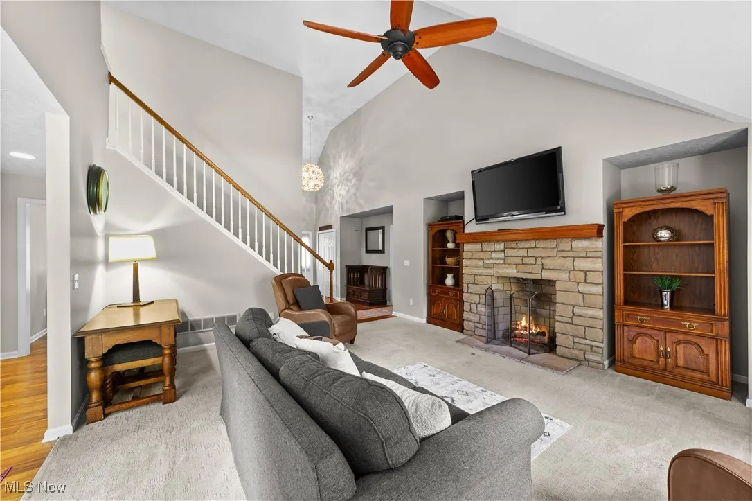 Carpeted living area featuring high vaulted ceiling, a fireplace, ceiling fan, and stairs