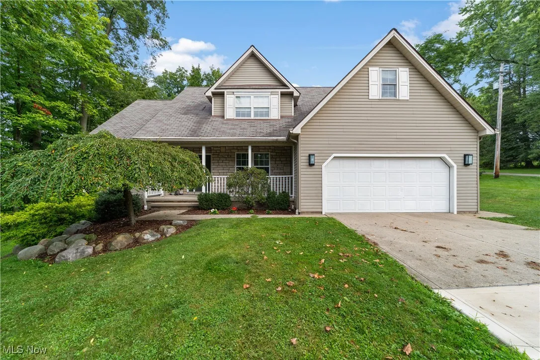 Traditional home with a porch, driveway, a front yard, a shingled roof, and an attached garage