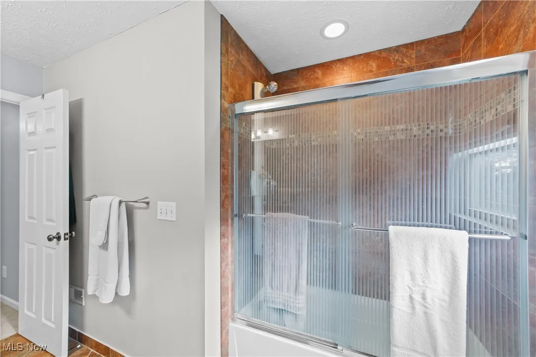 Bathroom with a textured ceiling, enclosed tub / shower combo, and tile patterned flooring