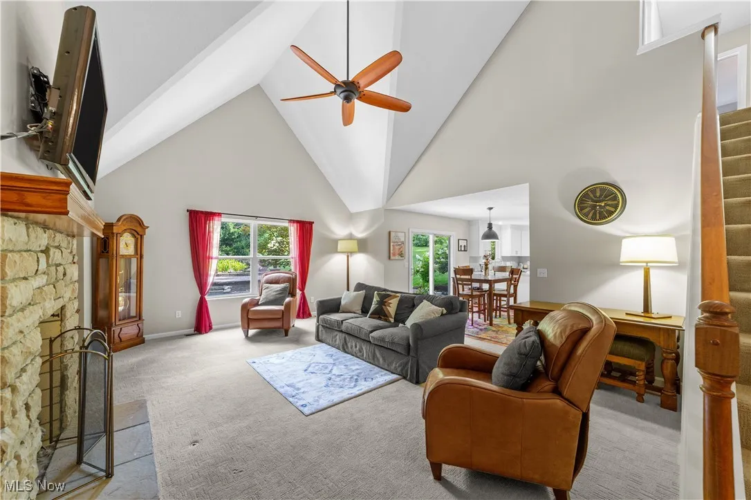 Living room featuring high vaulted ceiling, carpet flooring, stairway, a stone fireplace, and healthy amount of natural light