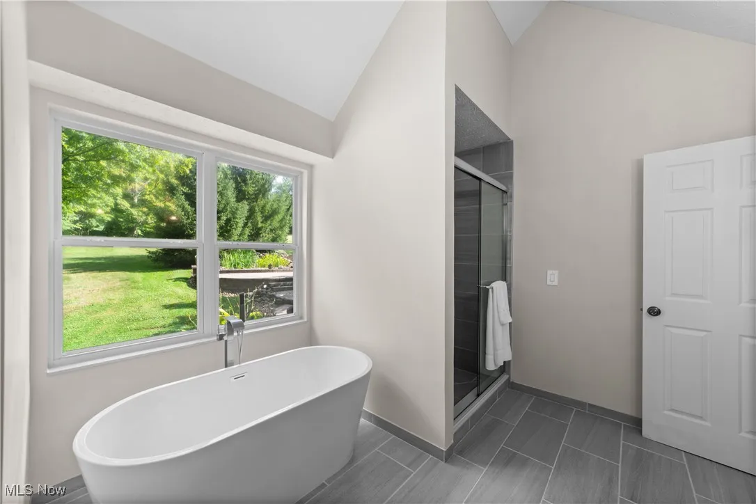 Full bathroom featuring a soaking tub, a shower stall, and vaulted ceiling