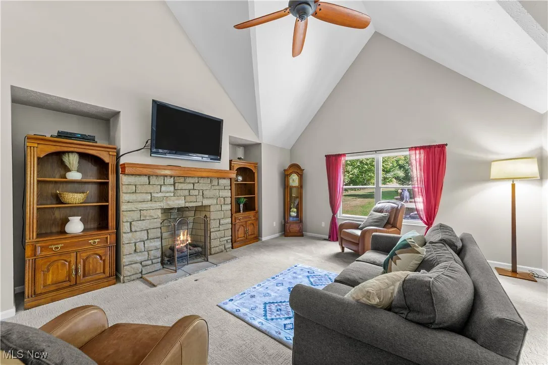 Carpeted living area with high vaulted ceiling, a fireplace, and ceiling fan