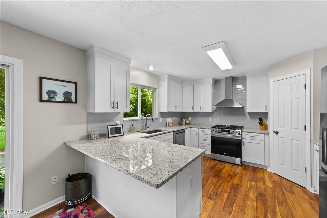 Kitchen with a peninsula, light stone countertops, dark wood-style floors, backsplash, and a textured ceiling