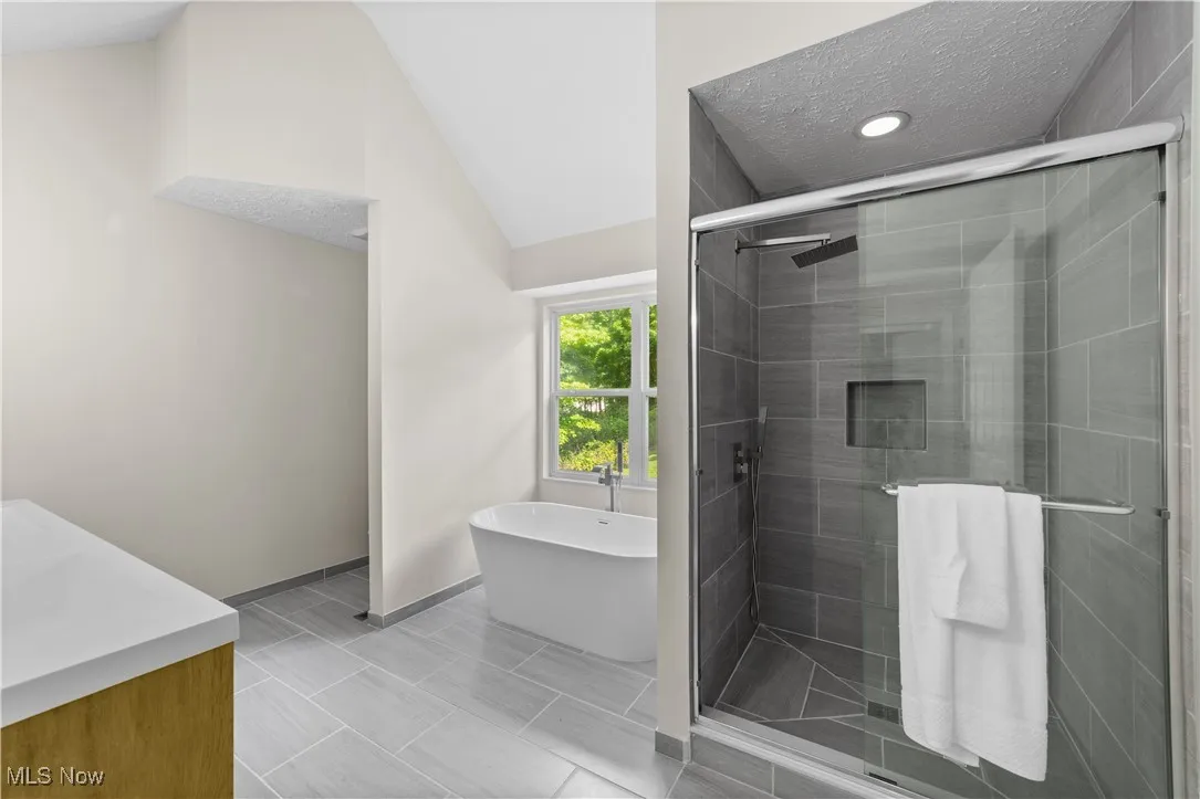 Full bath with vanity, vaulted ceiling, a textured ceiling, a soaking tub, and a shower stall