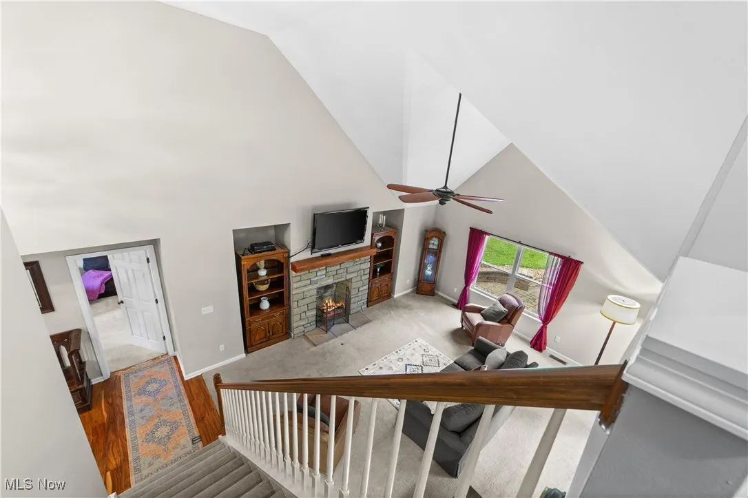 Staircase featuring high vaulted ceiling, a fireplace, wood finished floors, carpet flooring, and a ceiling fan