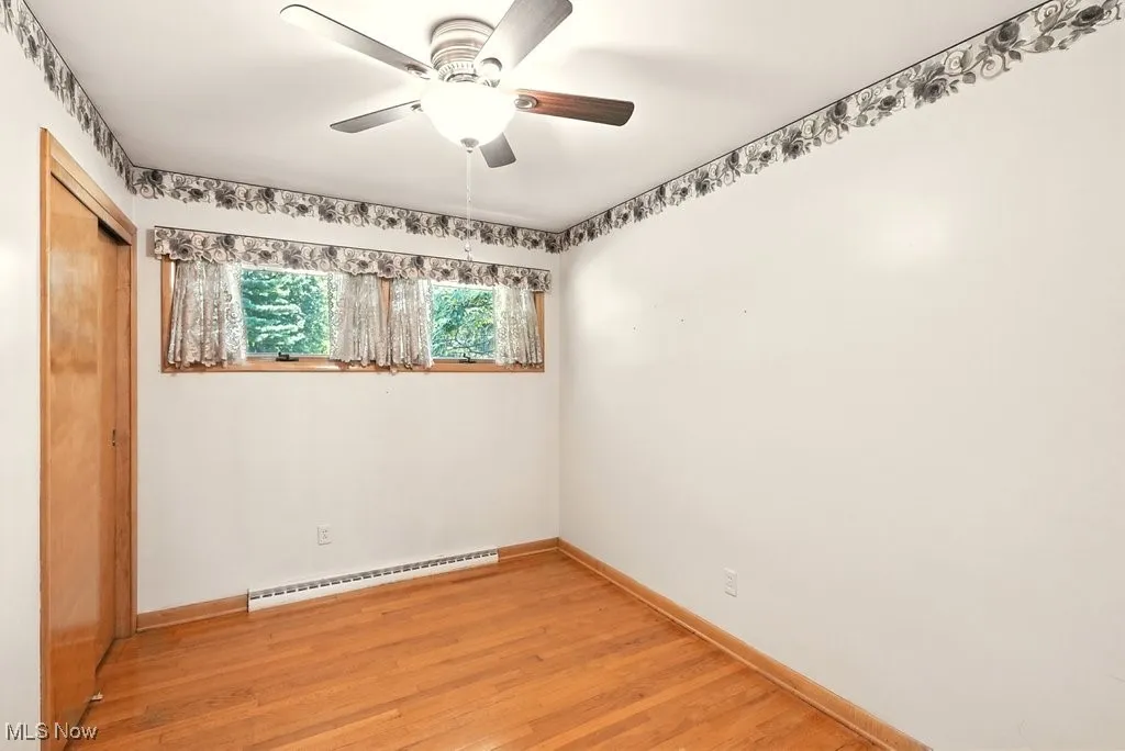 Unfurnished room featuring light wood-style floors, a baseboard heating unit, and a ceiling fan