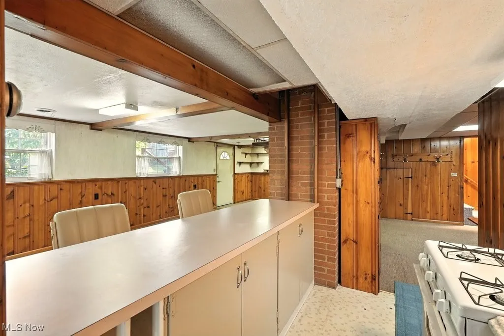 Kitchen with wood walls, white gas range, light countertops, light floors, and cream cabinetry