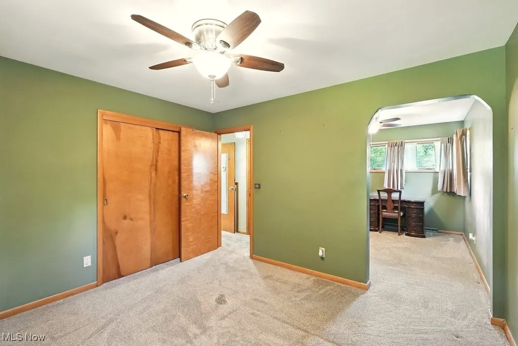 Unfurnished bedroom featuring carpet flooring, arched walkways, ceiling fan, and a closet