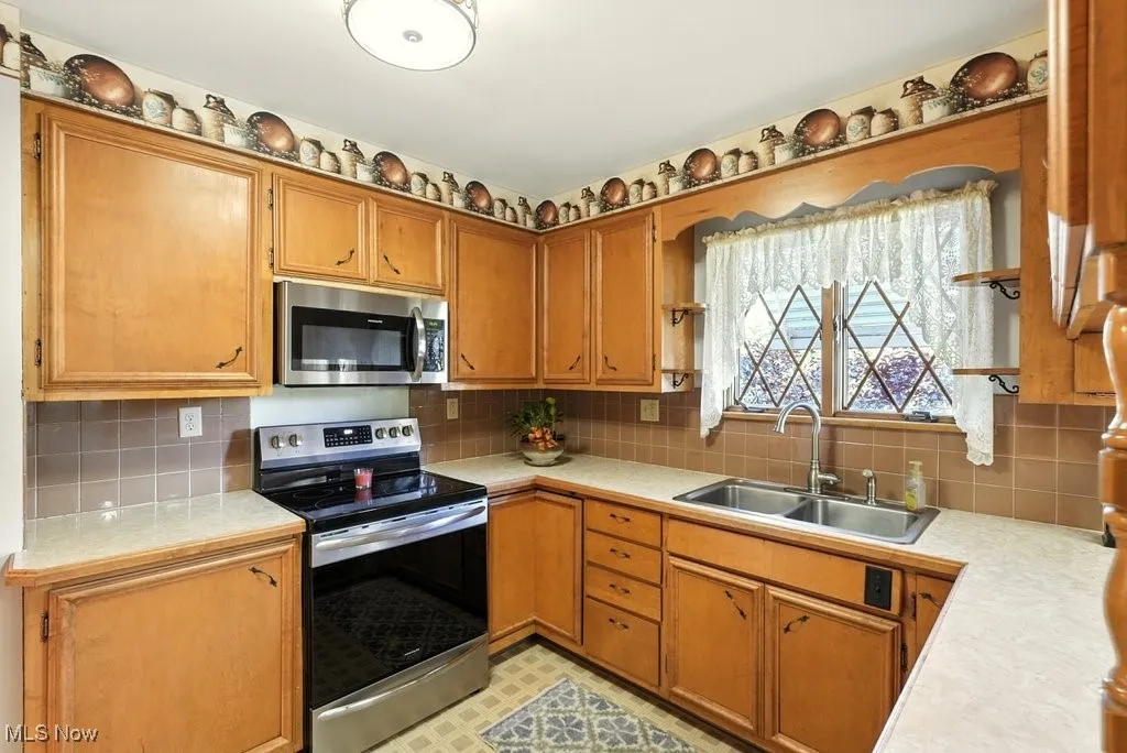 Kitchen with light countertops, stainless steel appliances, decorative backsplash, and brown cabinetry
