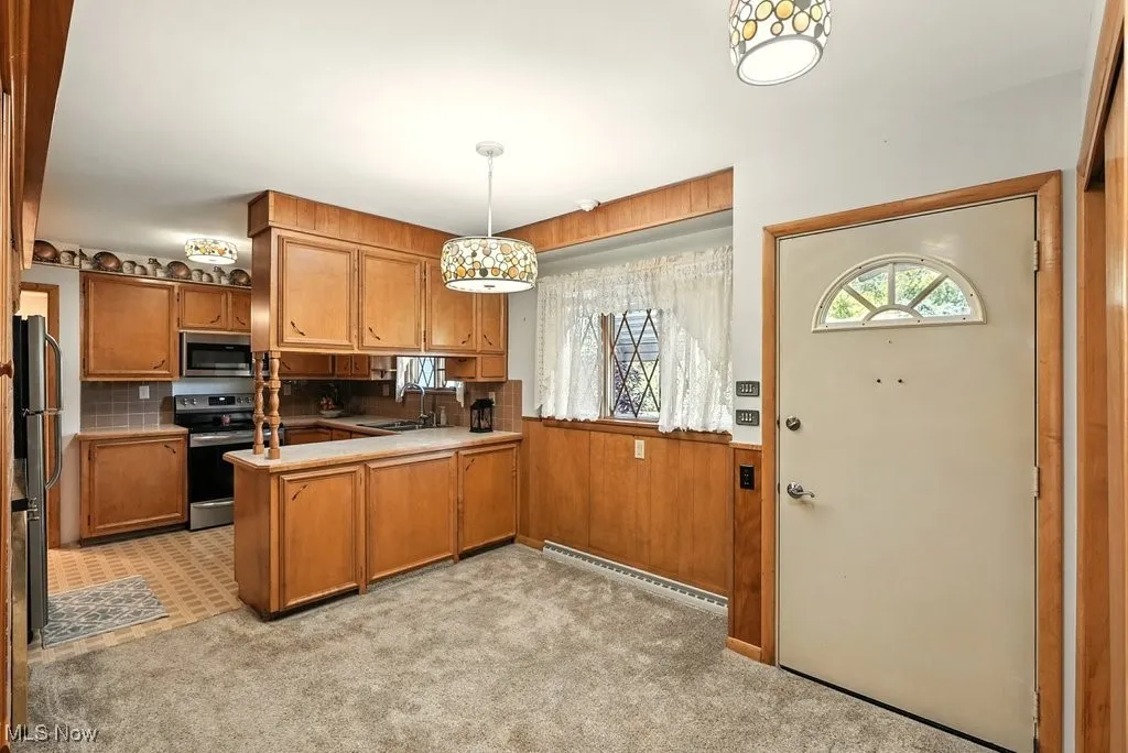 Kitchen with brown cabinets, decorative light fixtures, stainless steel appliances, a peninsula, and decorative backsplash