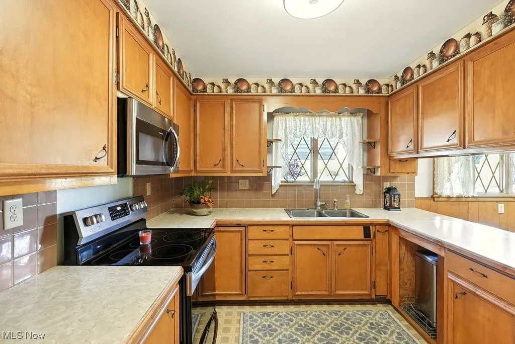 Kitchen featuring stainless steel appliances, backsplash, light countertops, and brown cabinetry