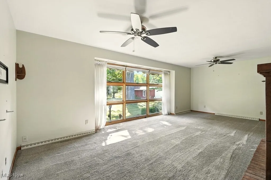 Carpeted spare room with baseboard heating and a ceiling fan