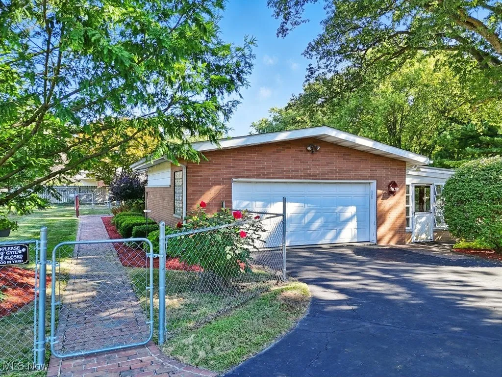 View of front of property with a garage, brick siding, asphalt driveway, and a gate