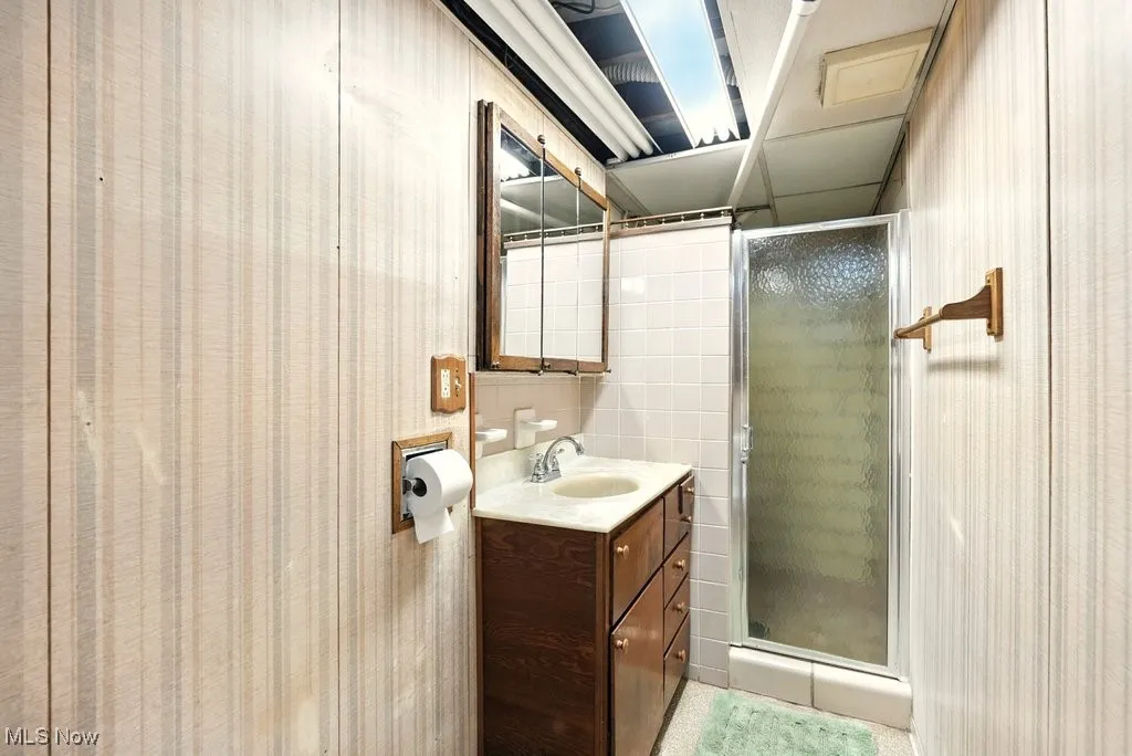 Full bathroom featuring a shower stall, vanity, and wallpapered walls