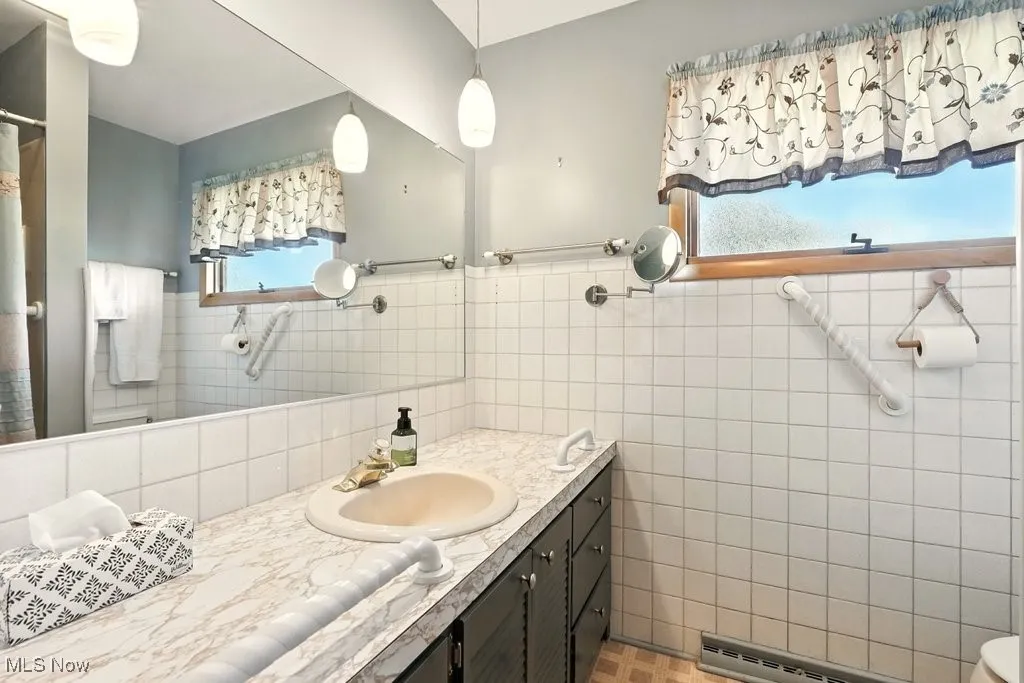 Full bathroom with tile walls, vanity, a baseboard radiator, wainscoting, and a shower with curtain