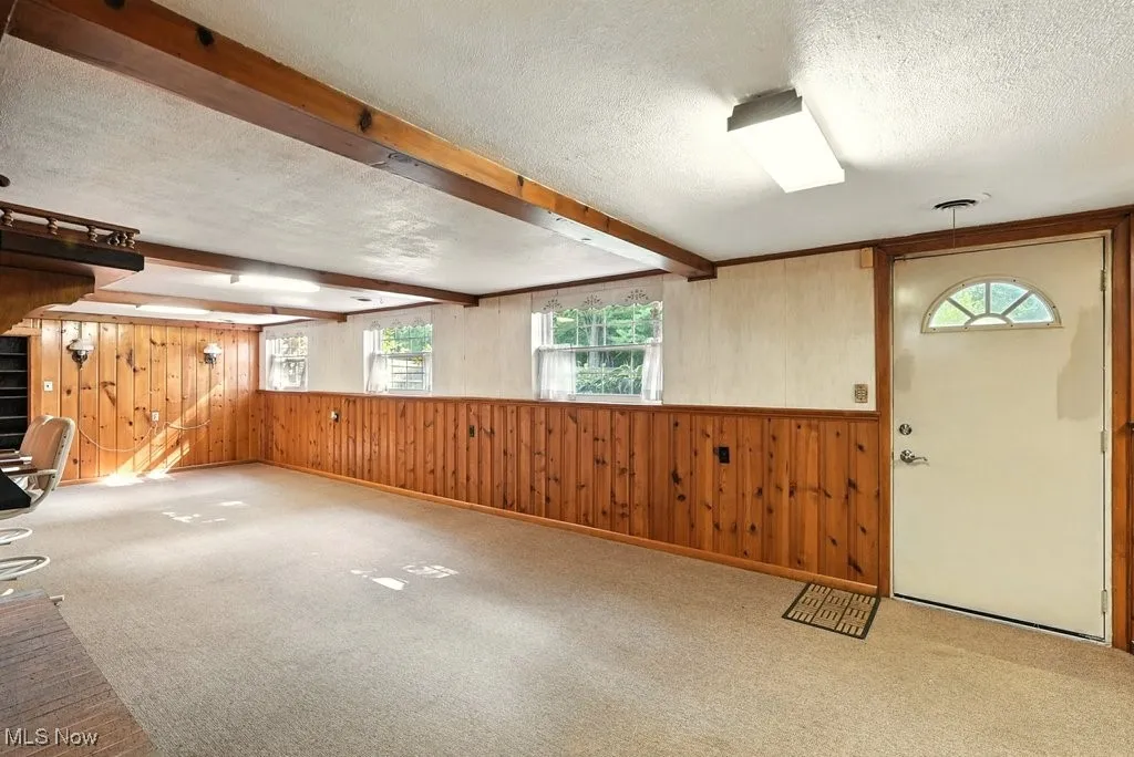 Entrance foyer with wooden walls, a textured ceiling, beamed ceiling, carpet flooring, and stairs