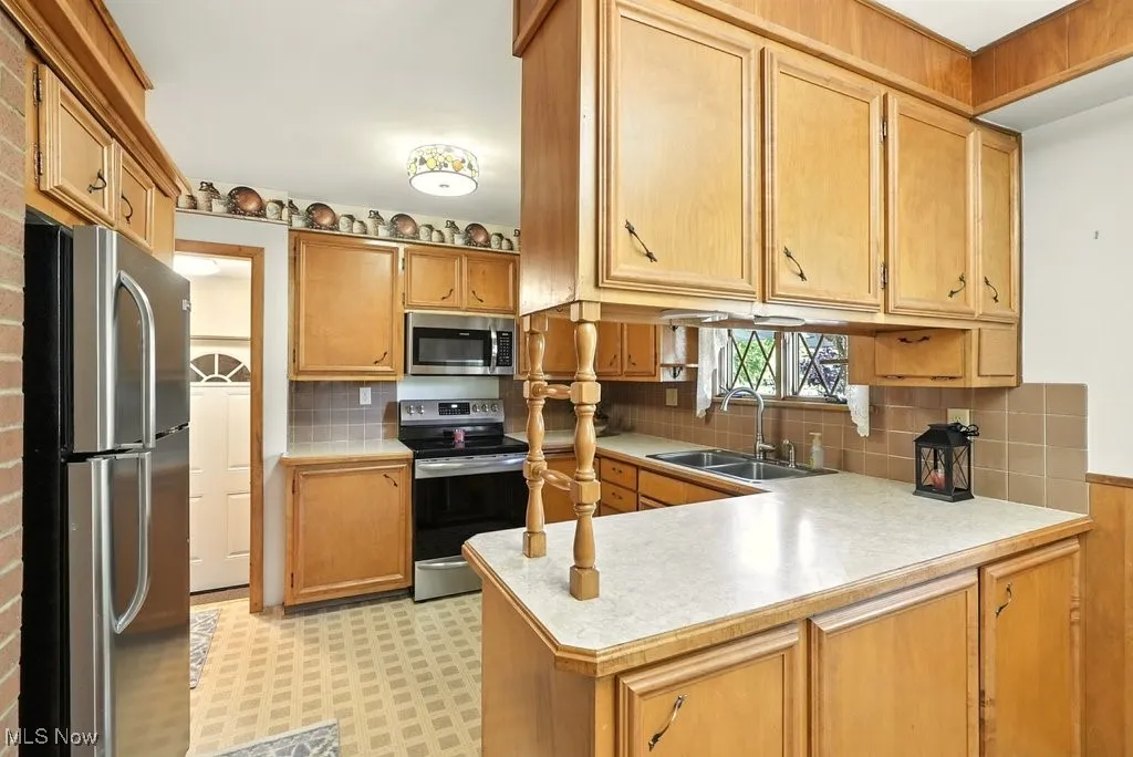 Kitchen with appliances with stainless steel finishes, light countertops, backsplash, a peninsula, and light floors