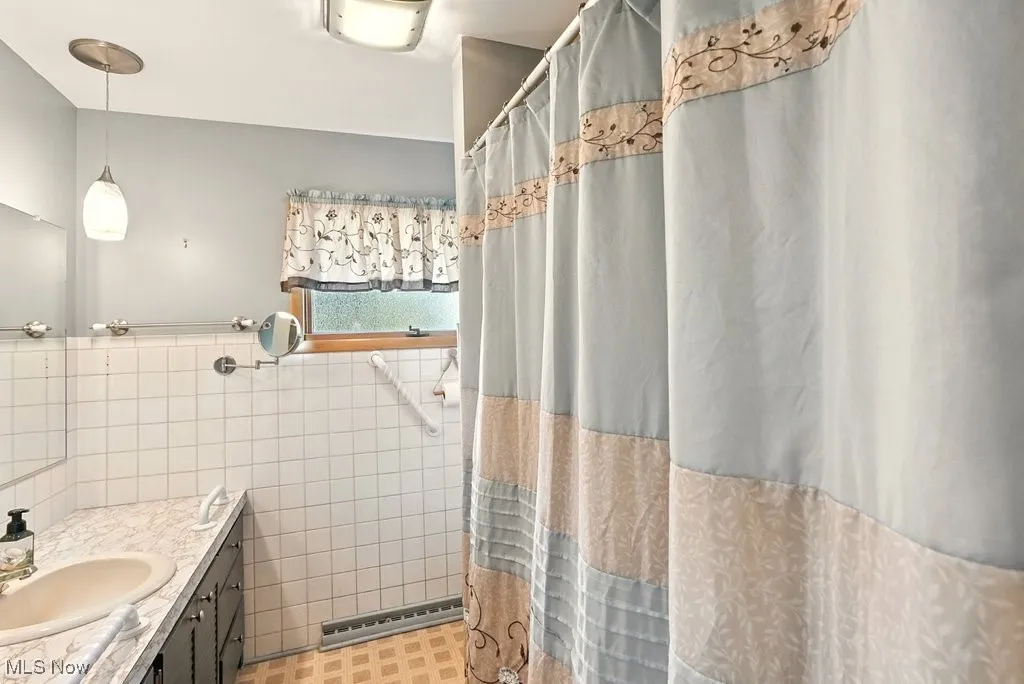 Full bath featuring tile walls, vanity, a shower stall, a wainscoted wall, and a baseboard radiator