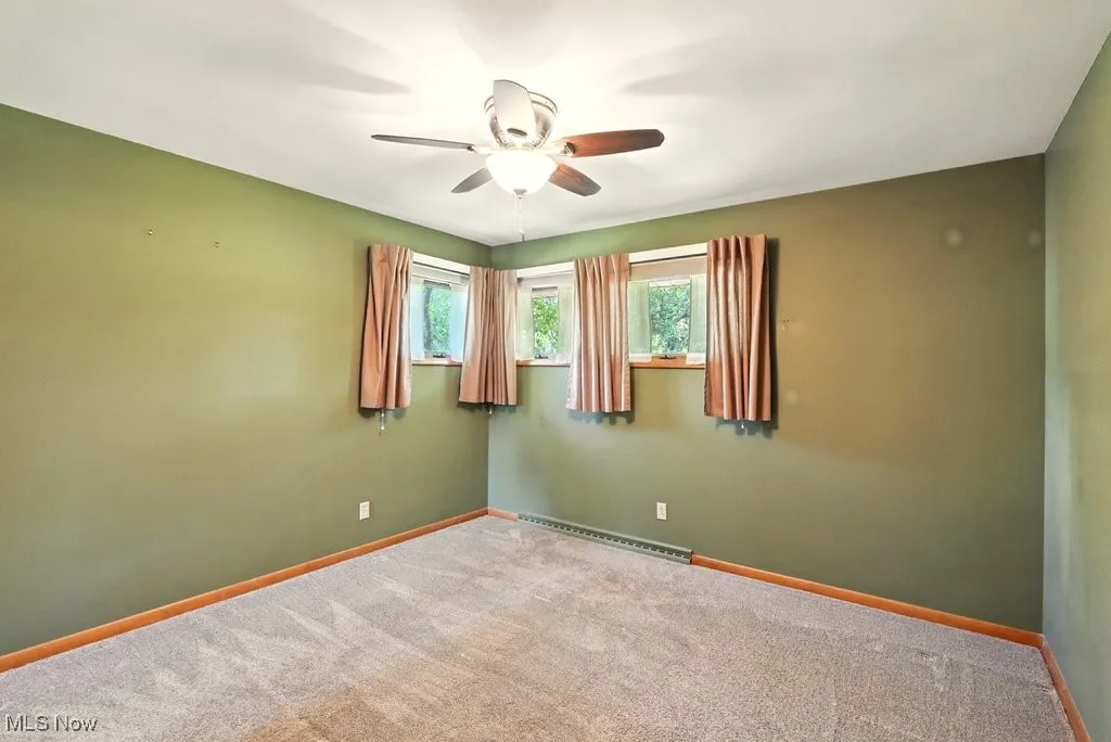 Empty room featuring carpet floors, ceiling fan, and a baseboard radiator