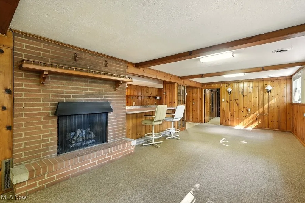 Bar featuring beam ceiling, a brick fireplace, carpet flooring, and wooden walls