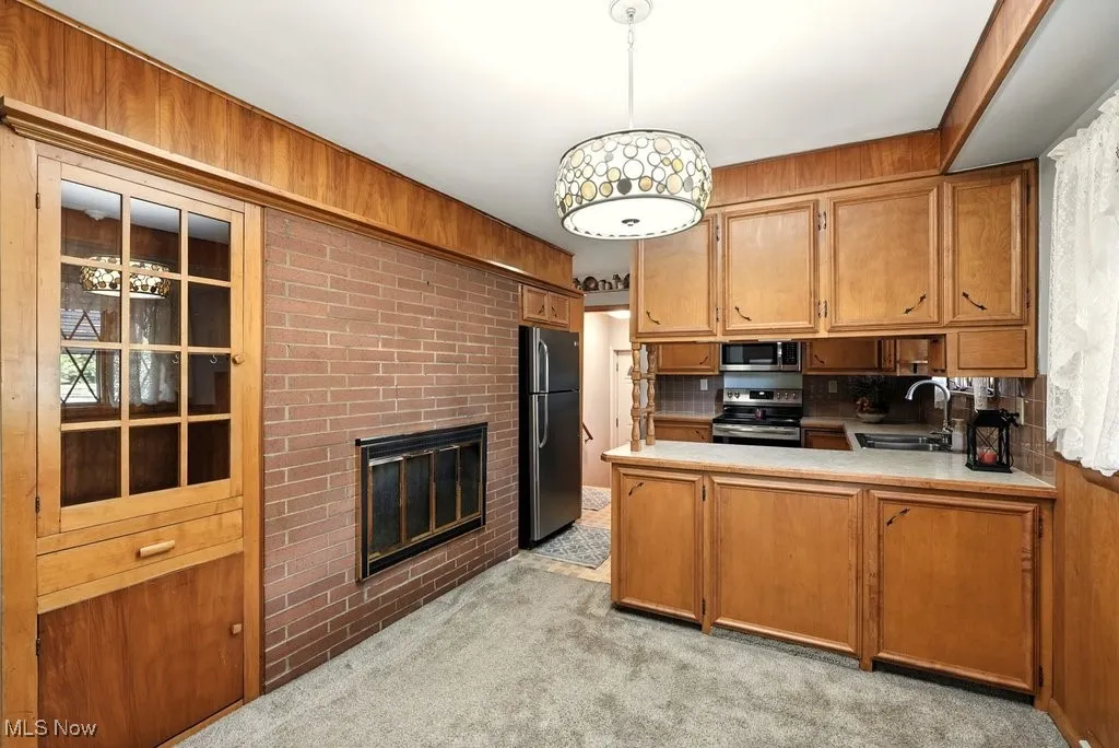 Kitchen with light colored carpet, decorative light fixtures, light countertops, brown cabinetry, and a fireplace
