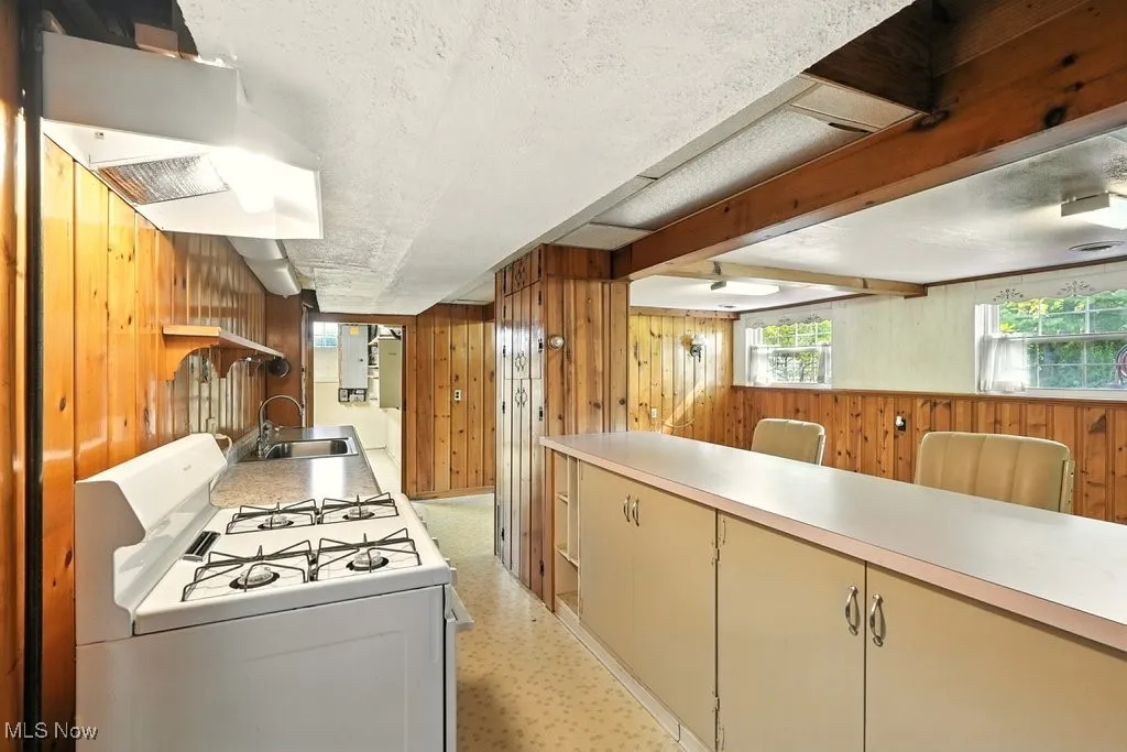 Kitchen with wooden walls, white gas range, extractor fan, light countertops, and a textured ceiling
