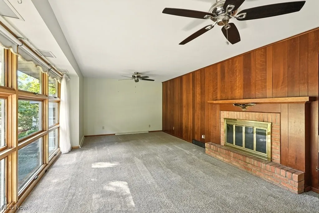 Unfurnished living room with wood walls, a brick fireplace, carpet floors, and ceiling fan