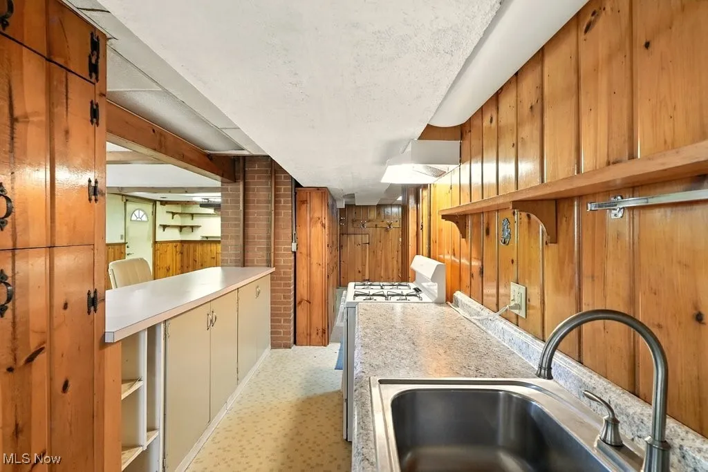 Kitchen with white gas range, wood walls, light countertops, and wall chimney exhaust hood