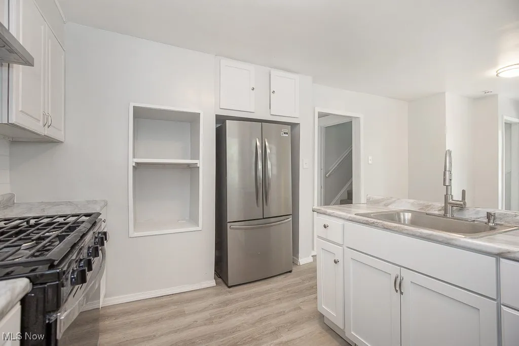 Kitchen featuring freestanding refrigerator, white cabinets, light countertops, light wood-style flooring, and black gas range