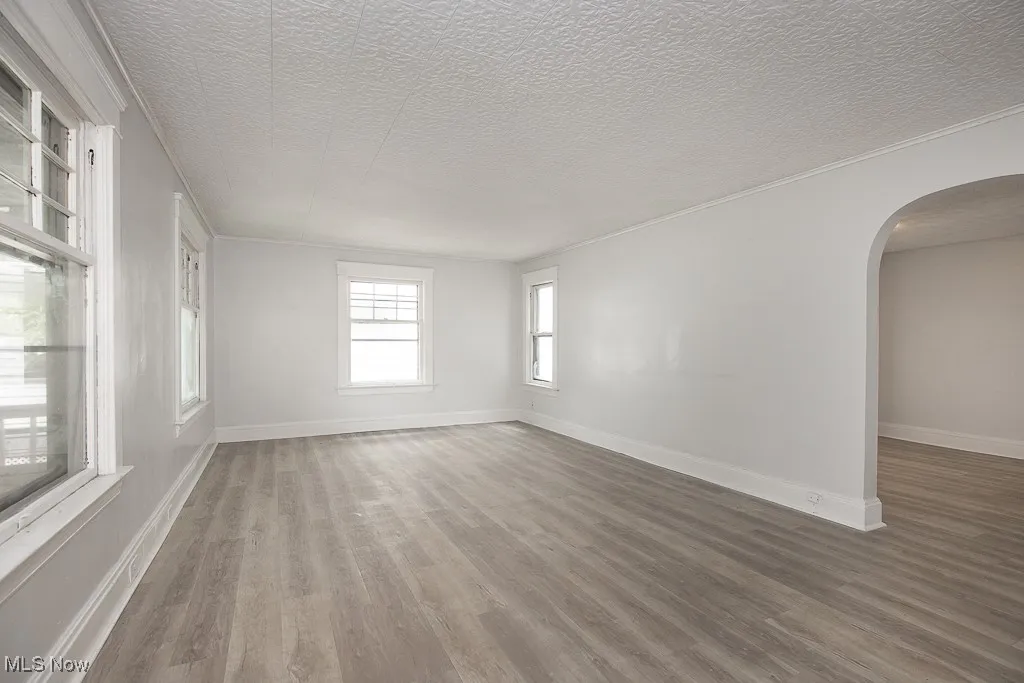 Unfurnished room featuring arched walkways, light wood-type flooring, a textured ceiling, and crown molding