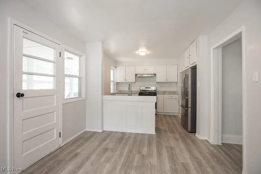 Kitchen featuring decorative backsplash, white cabinets, stainless steel appliances, light wood-style floors, and light countertops