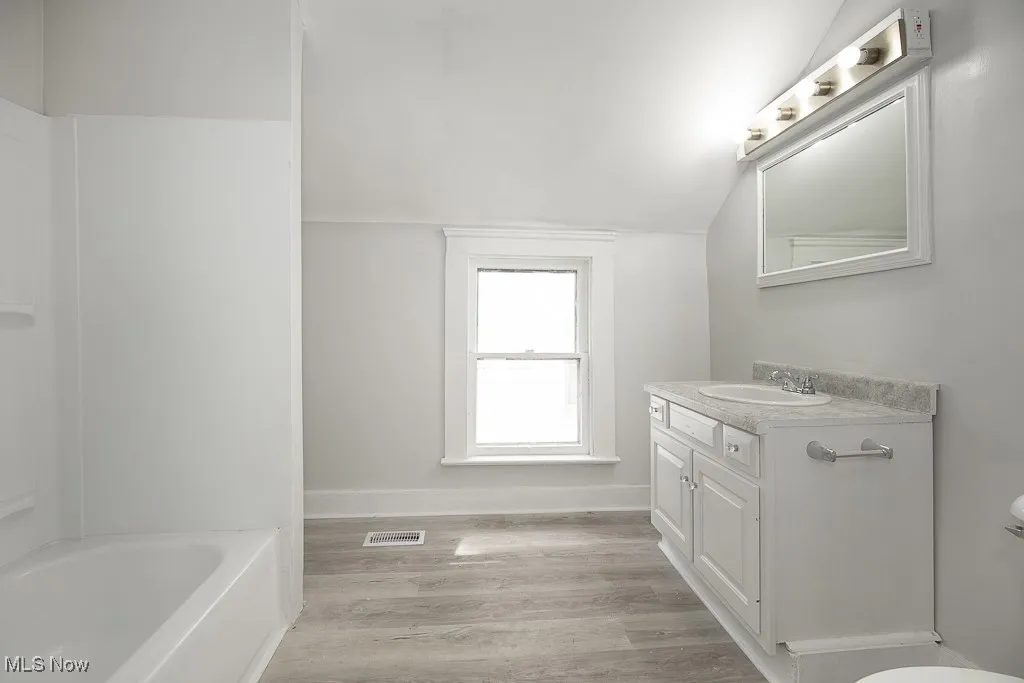 Bathroom featuring vanity, light wood-type flooring, vaulted ceiling, and bathtub / shower combination