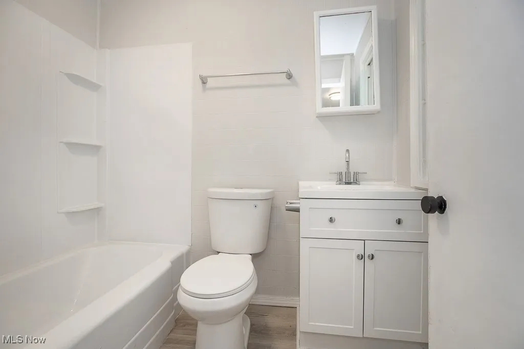 Bathroom featuring wood finished floors, vanity, tile walls, and washtub / shower combination