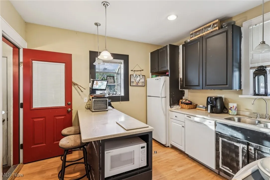 Kitchen featuring a kitchen bar, white appliances, light wood finished floors, decorative light fixtures, and recessed lighting